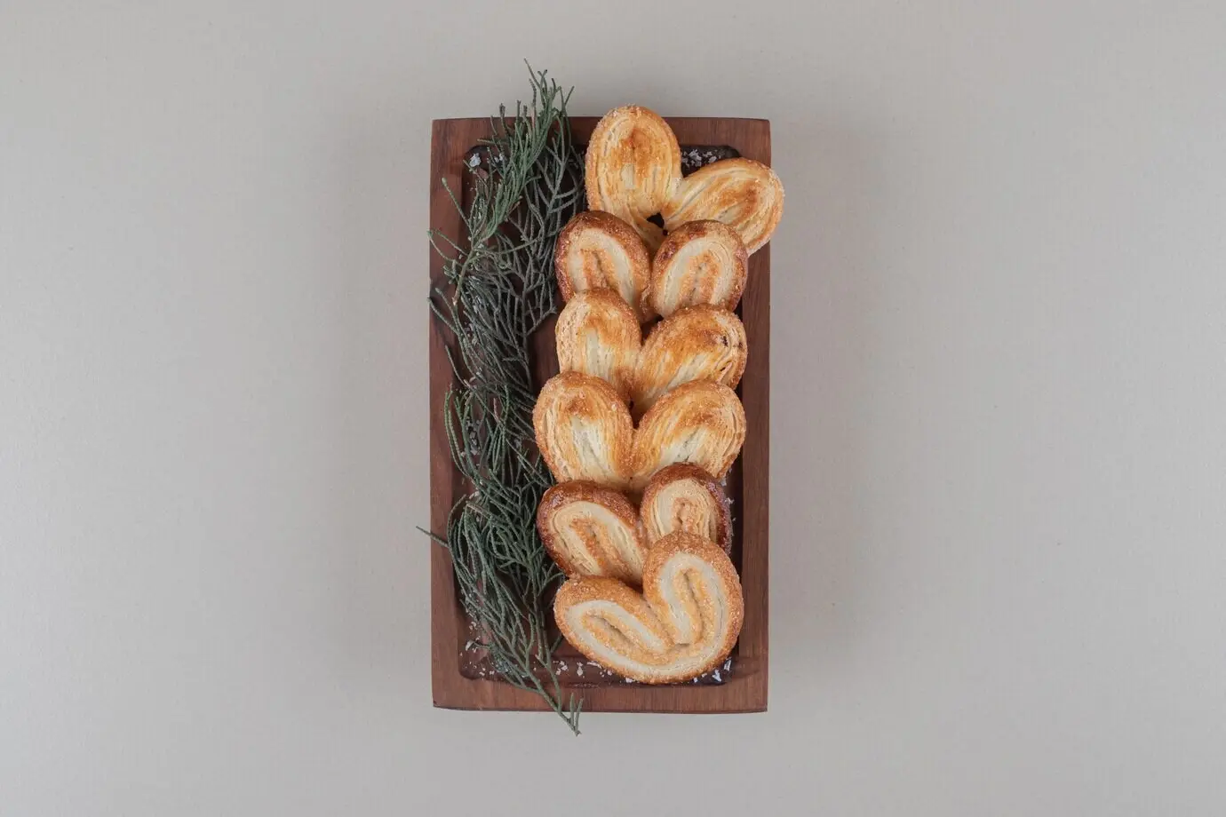 Blättrige Kekse, auf einem kleinen Holztablett mit einem Bündel Kiefernnadeln aufgereiht, vor Marmorhintergrund.